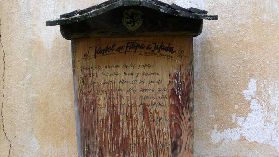 Dřevěná deska na zdi kostela připomíná všechny jeho přestavby