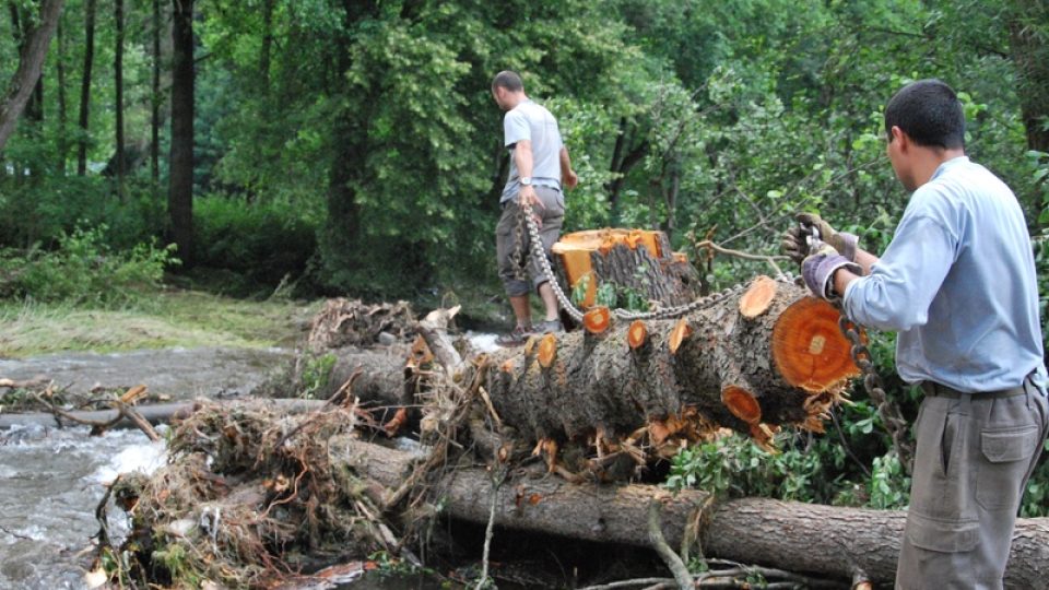 Vojáci s pomocí těžké techniky tahají napadané kmeny z potoka