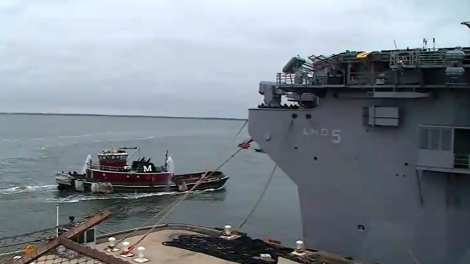 Do doku přijíždějí remorkéry, aby pomohly obřímu vojenskému kolosu opustit námořní základnu v Norfolku