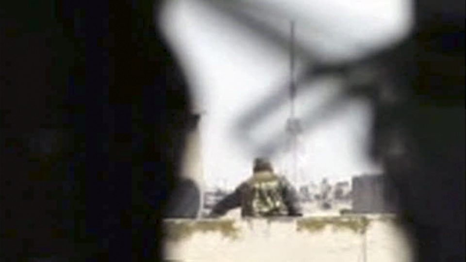 Sýrie. Muž ve vojenských maskáčích na střeše ve městě Homs zachycený amatérskou videokamerou během ostřelování civilistů