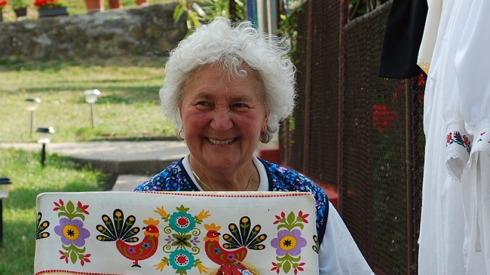 Starší žena vystavuje několik panenek oblečených do vyšívaných krojů
