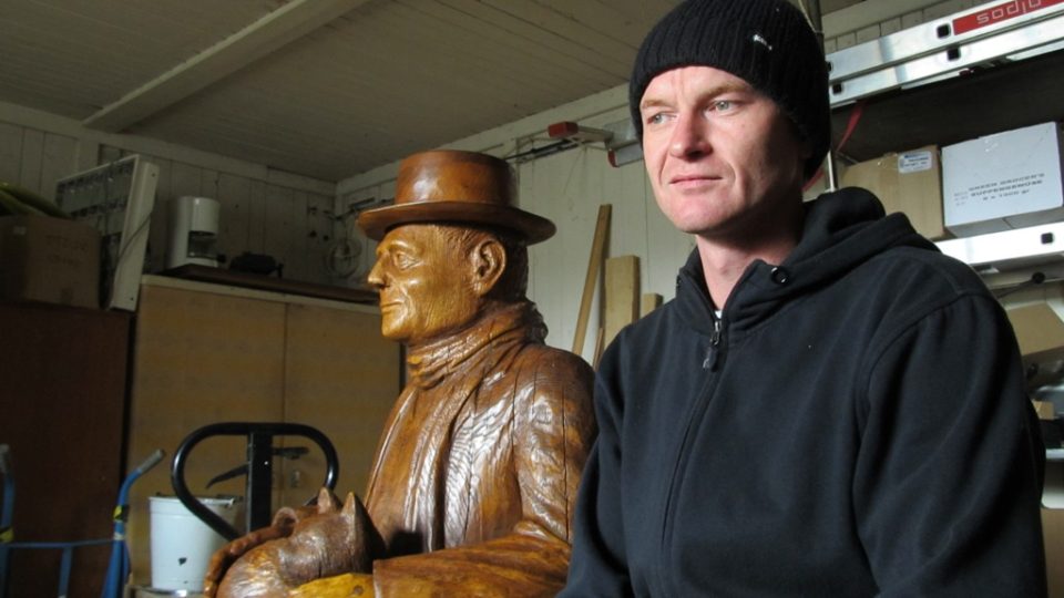 Michal Jára sedí vedle svého nového uměleckého díla - dřevěné sochy Bohumila Hrabala