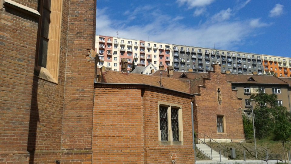 Kontrastní kulisu kostelu dělají adamovské panelové domy