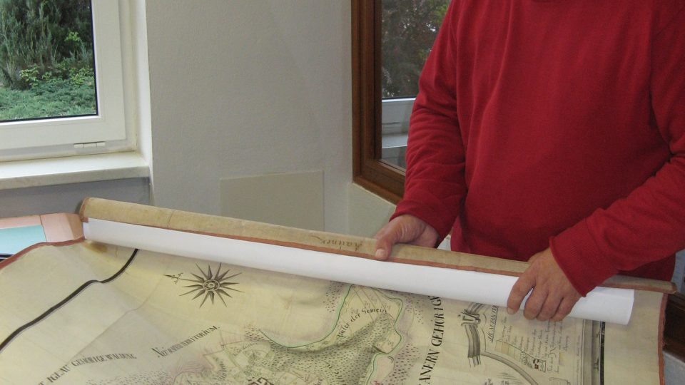 Archivář Vlastimil Svěrák rozbaluje ručně malovanou mapu z 18. století
