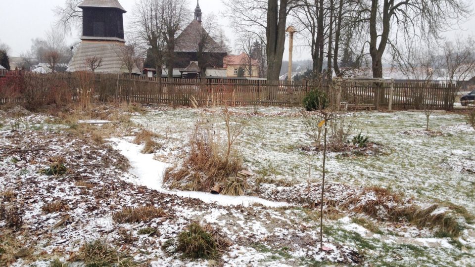 Přírodní zahrada se zamrzlým umělým potokem a kostelem ve Velinách v pozadí