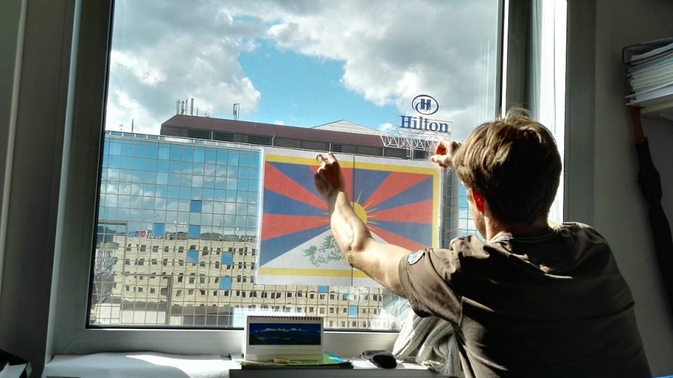 Vyvěšování tibetské vlajky v kanceláři naproti hotelu Hilton