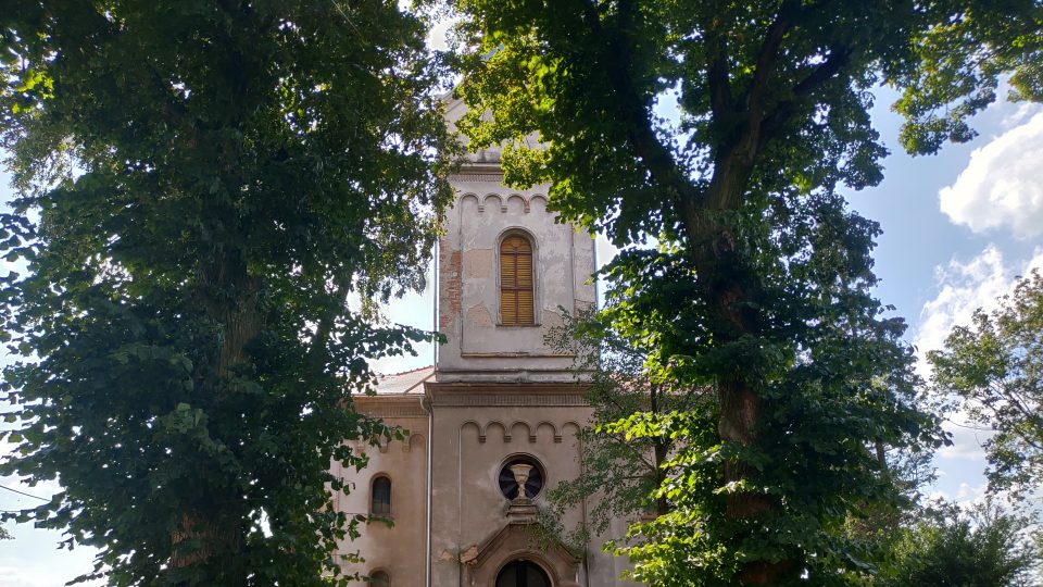 Z hlavní silnice není evangelický kostel skoro vidět. Zakrývají ho vzrostlé stromy